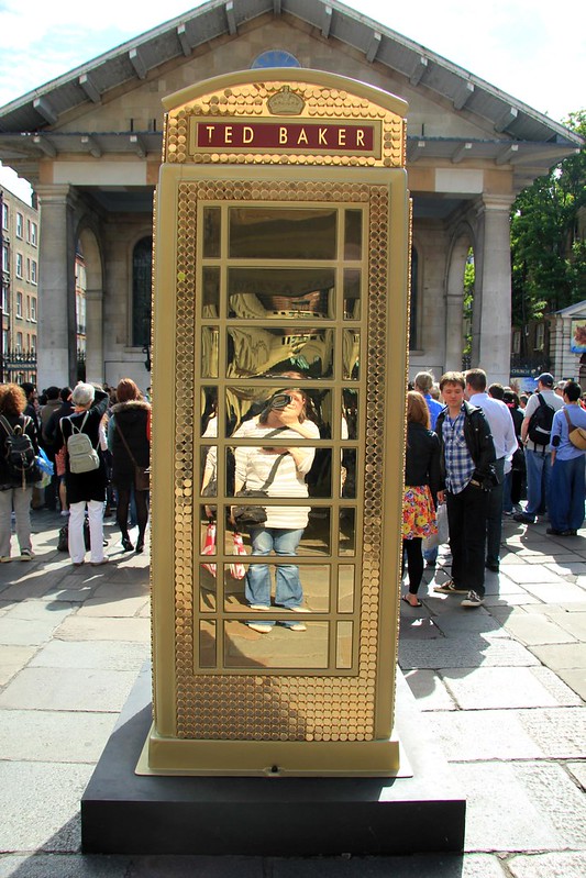 A British telephone box with golden Ted Baker branding.
